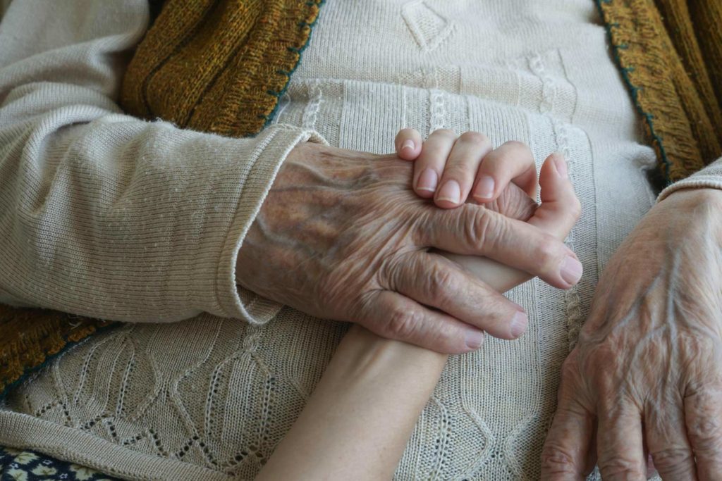 closeup wrinkled hand holding a younger hand
