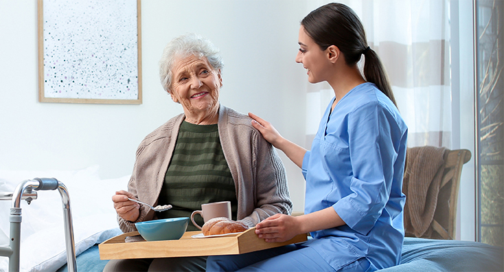 home Care worker serving dinner for elderly woman on geriatric hospice