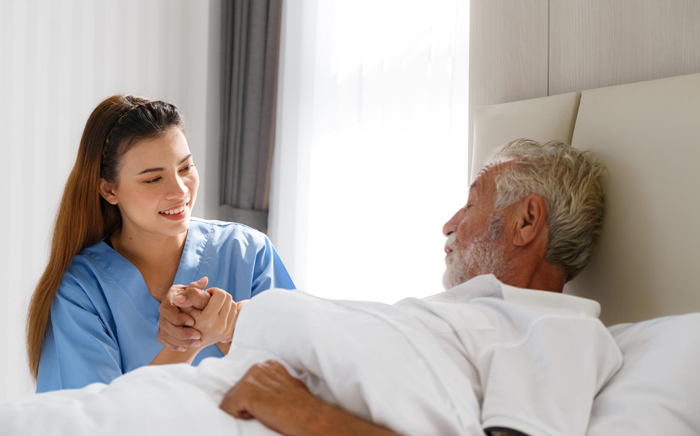 Care taker holding senior patient's hand bedside